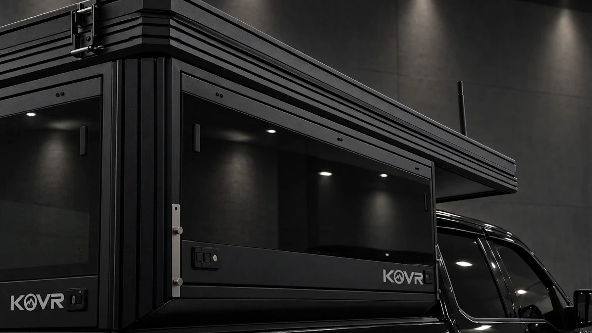 Gros plan d'un campeur KOVR : panneaux d'aluminium noir Powder Coated, cadre de la fenêtre panoramique, loquets et charnières, et écusson KOVR