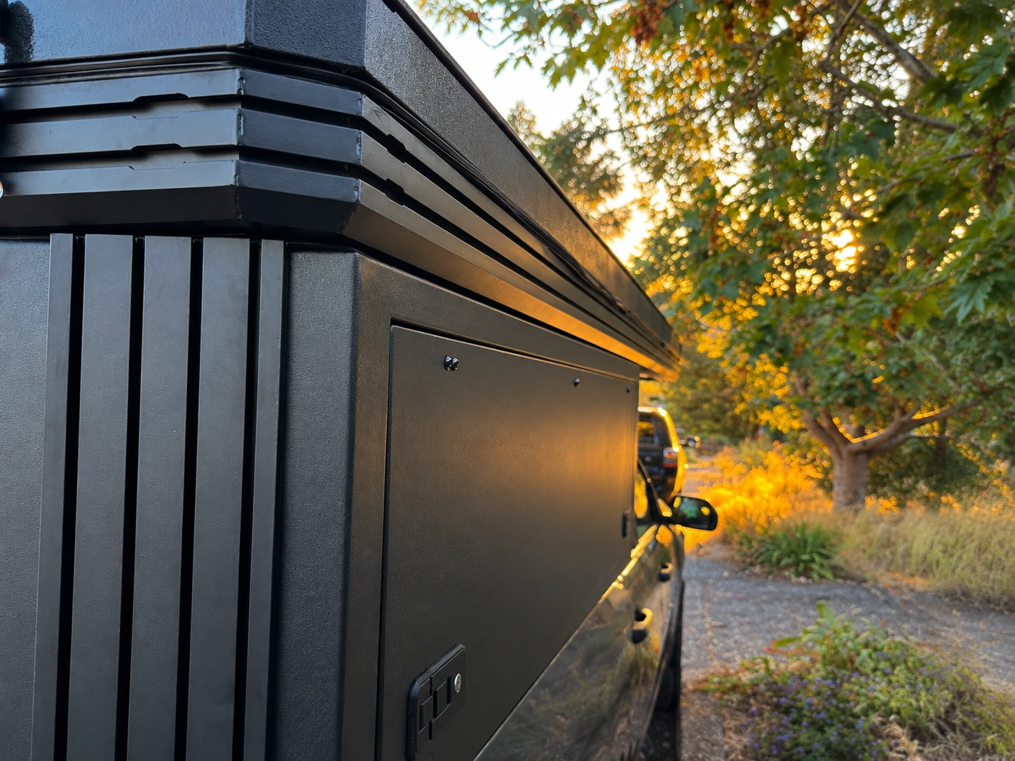 Gros plan d'un KOVR XL1 noir, modèle de base, au coucher du soleil : rails en T le long du toit, panneaux d'aluminium Powder Coated et loquet verrouillable